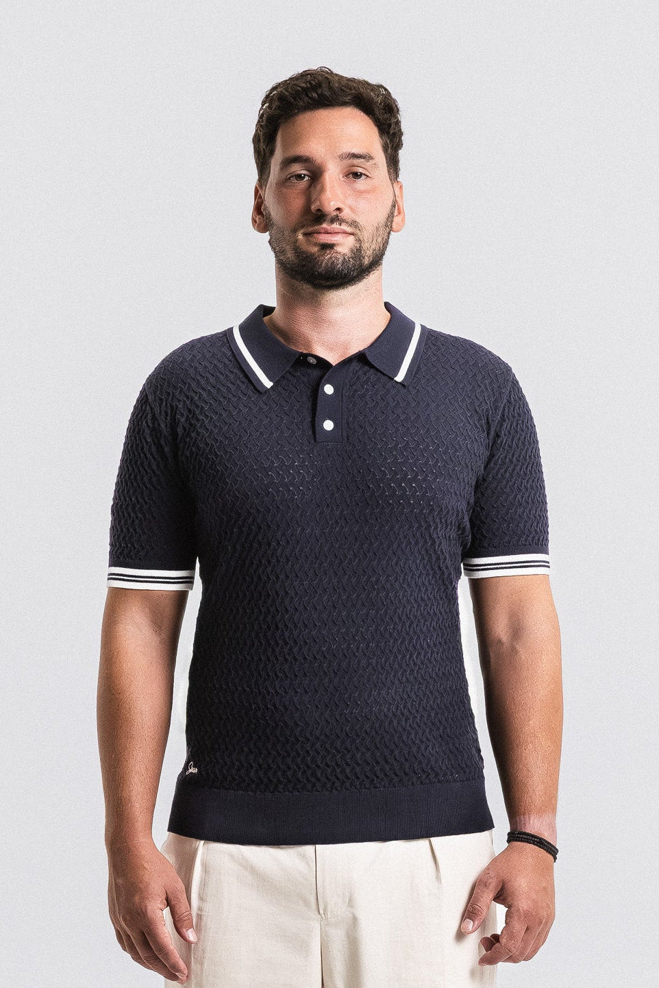 Man wearing a navy blue textured polo shirt with white accents on a light gray background