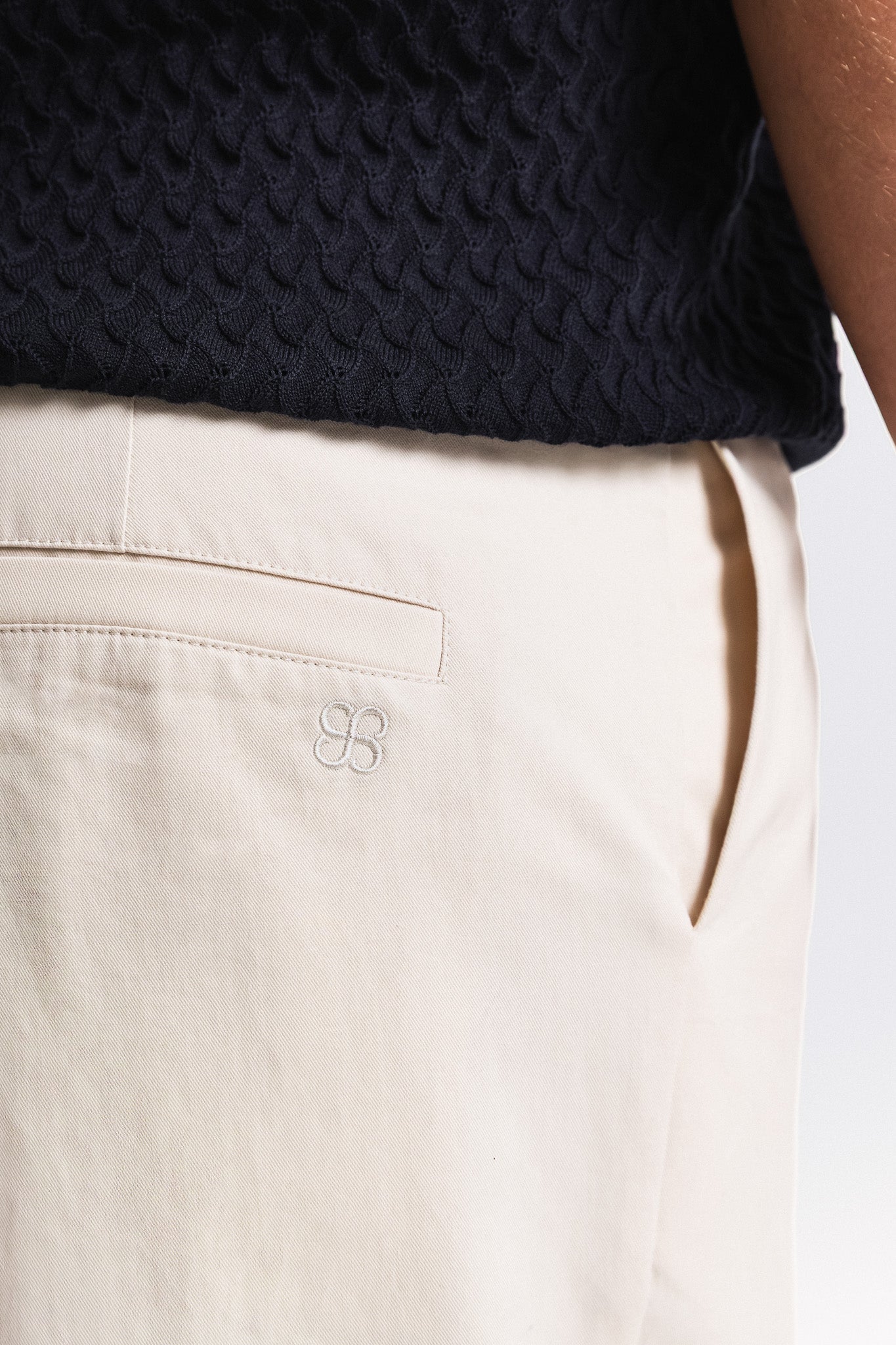 Close-up of beige pants with a brand logo on a white background