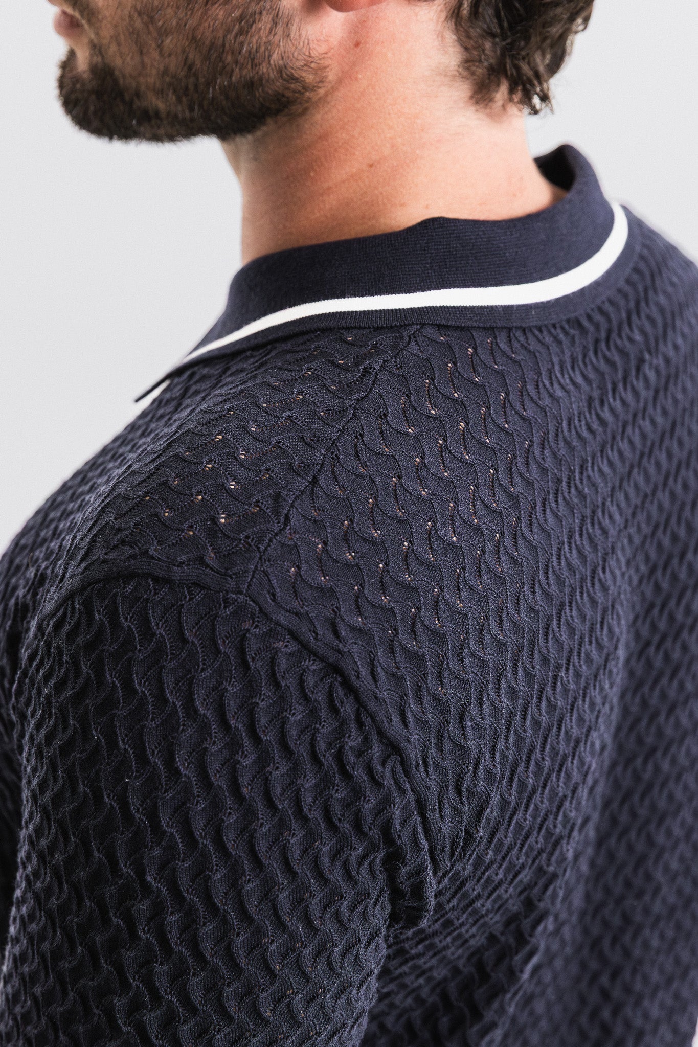 Navy blue textured sweater with white trim on a light gray background