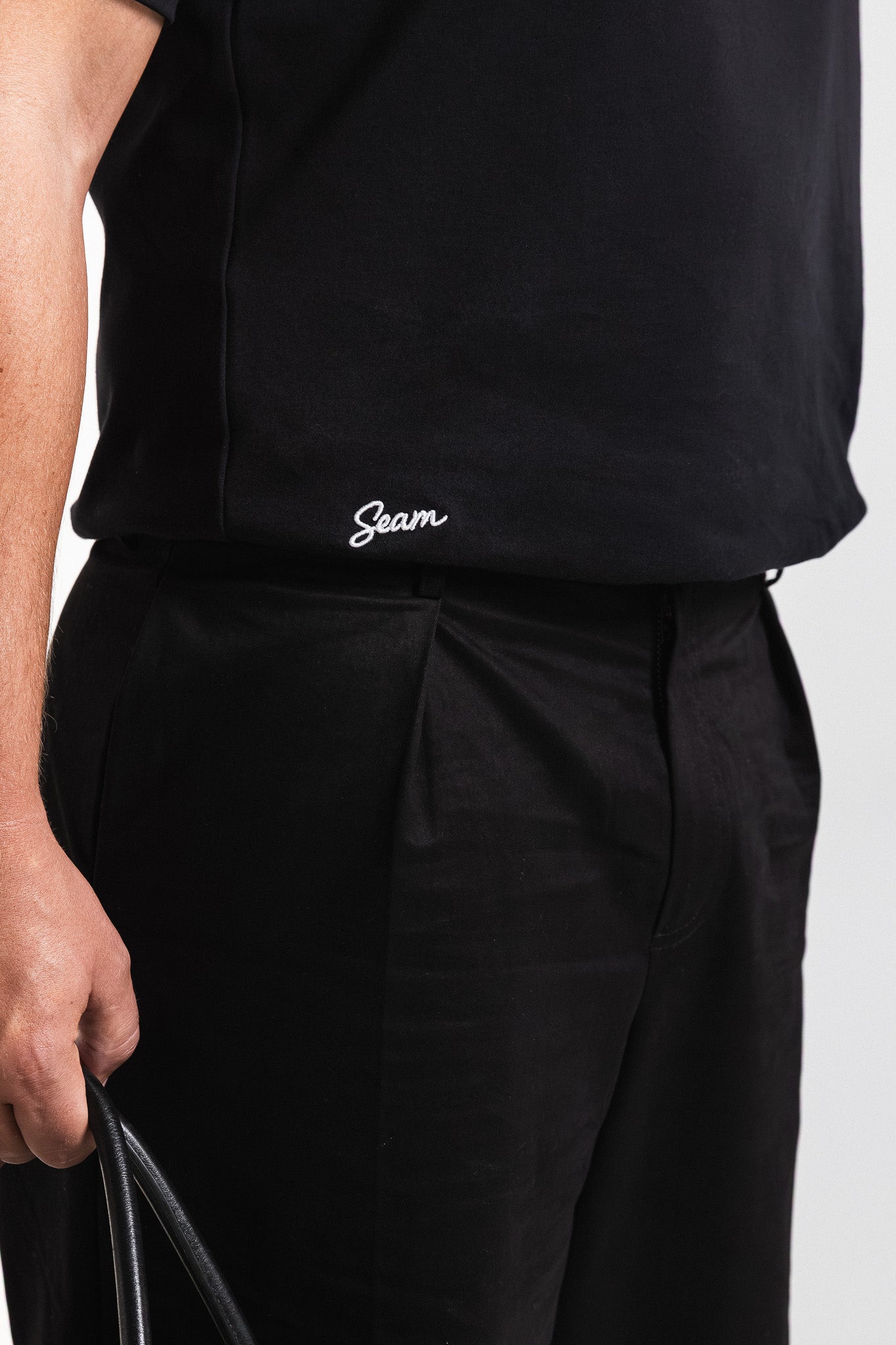 Person wearing a black outfit with 'Seam' embroidery on a plain background