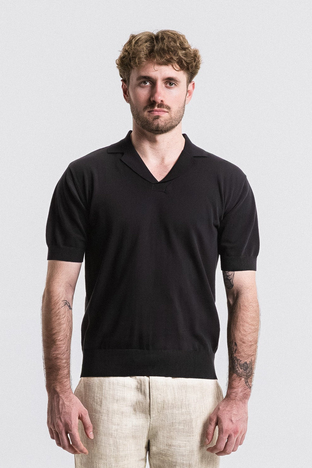 Man wearing a black V-neck shirt and beige pants against a white background