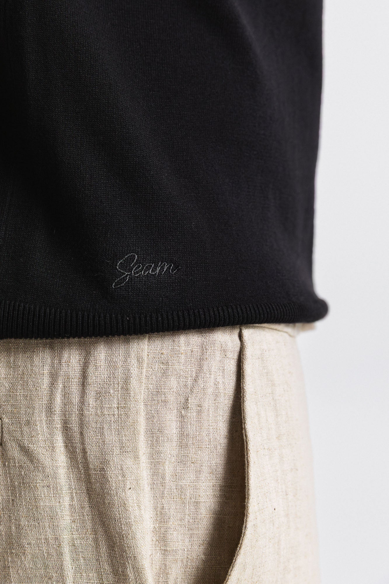 Close-up of a black sweater with 'Seam' branding on a light background