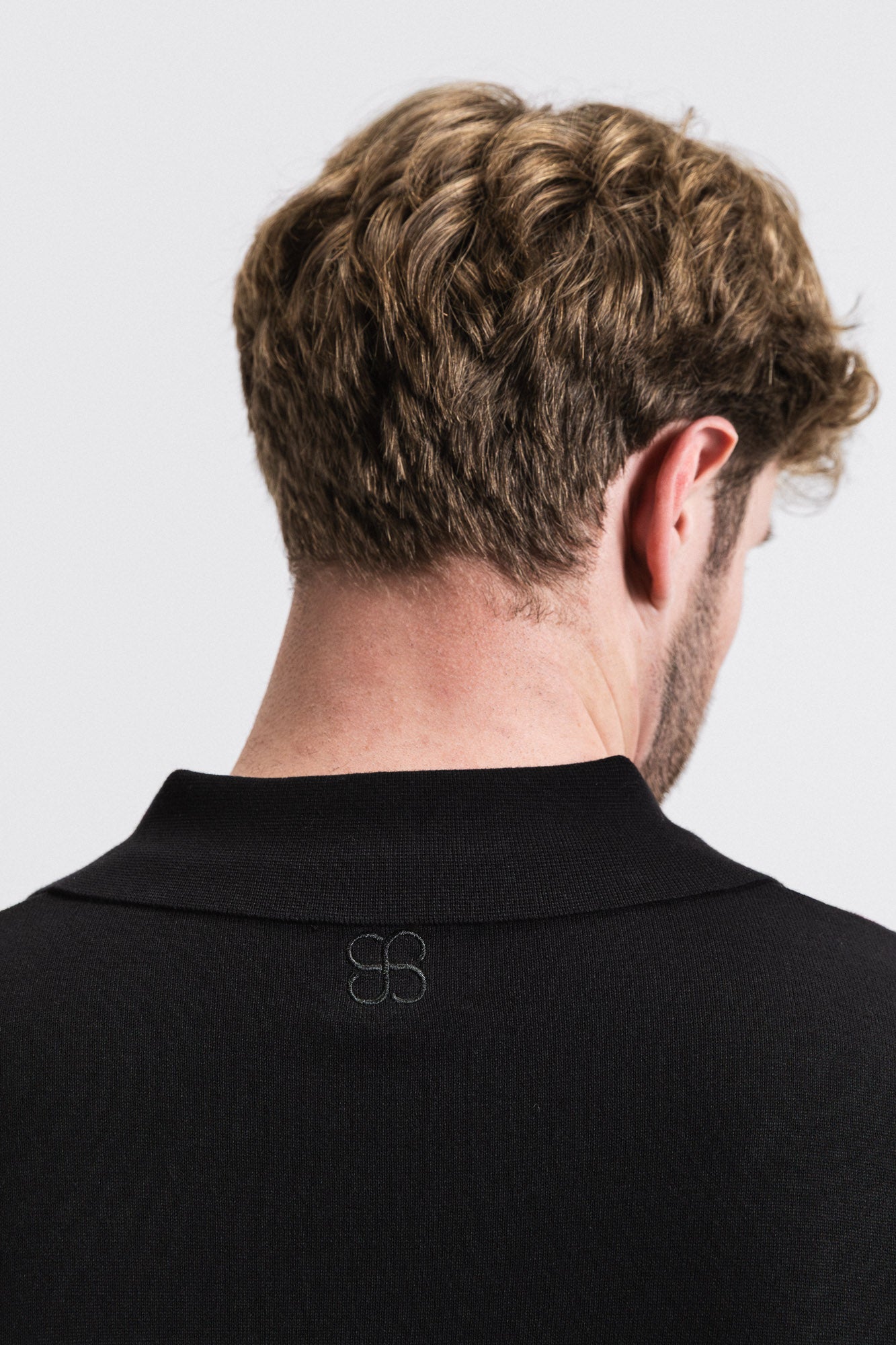 Man wearing a black polo shirt with a logo on the back against a white background