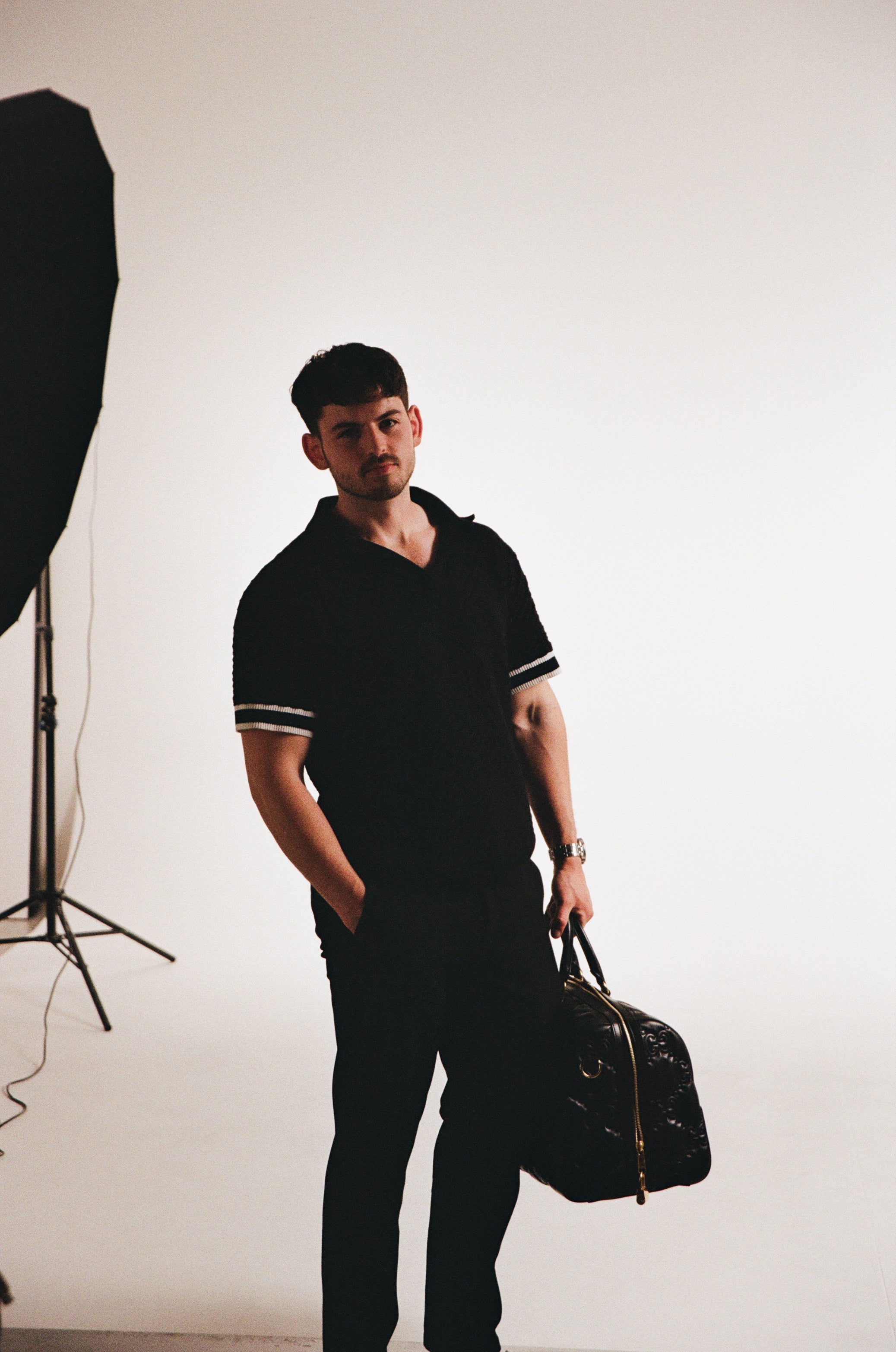 Man in a black outfit with a cap holding a guitar in a studio setting