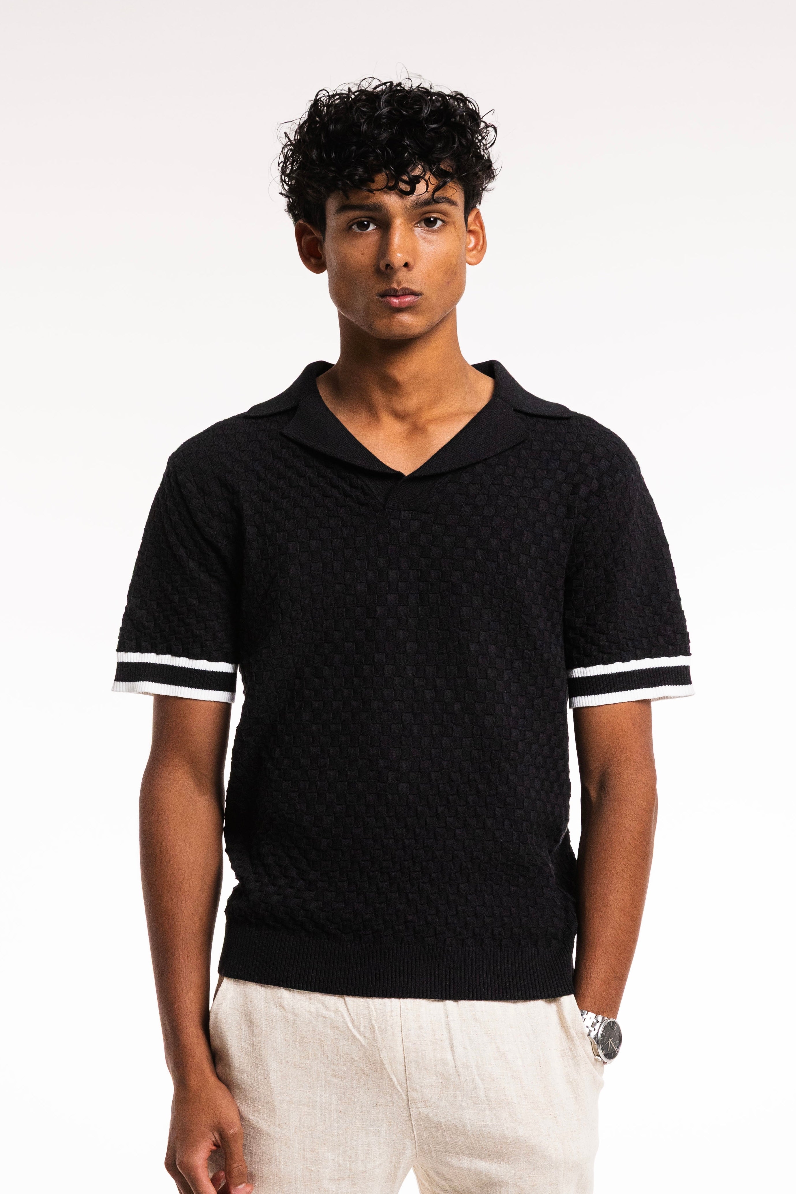 Model wearing Checkered Cotton Knit Polo in Obsidian with sleek collar and contrast sleeve stripes.
