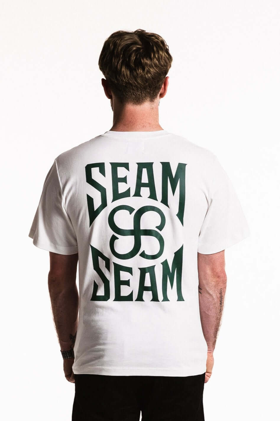 Back view of a man wearing a Cotton Typeface T-Shirt in white featuring bold SEAM branding.