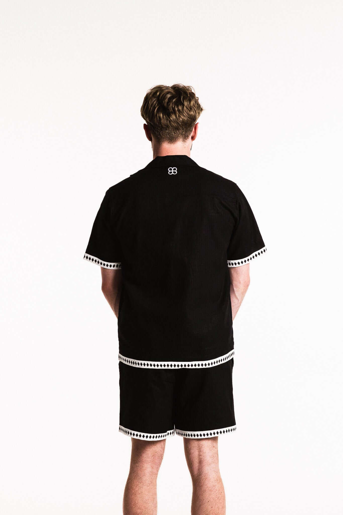 Back view of Diamond Trim Linen Shirt in black with white trim, styled casually with matching shorts.