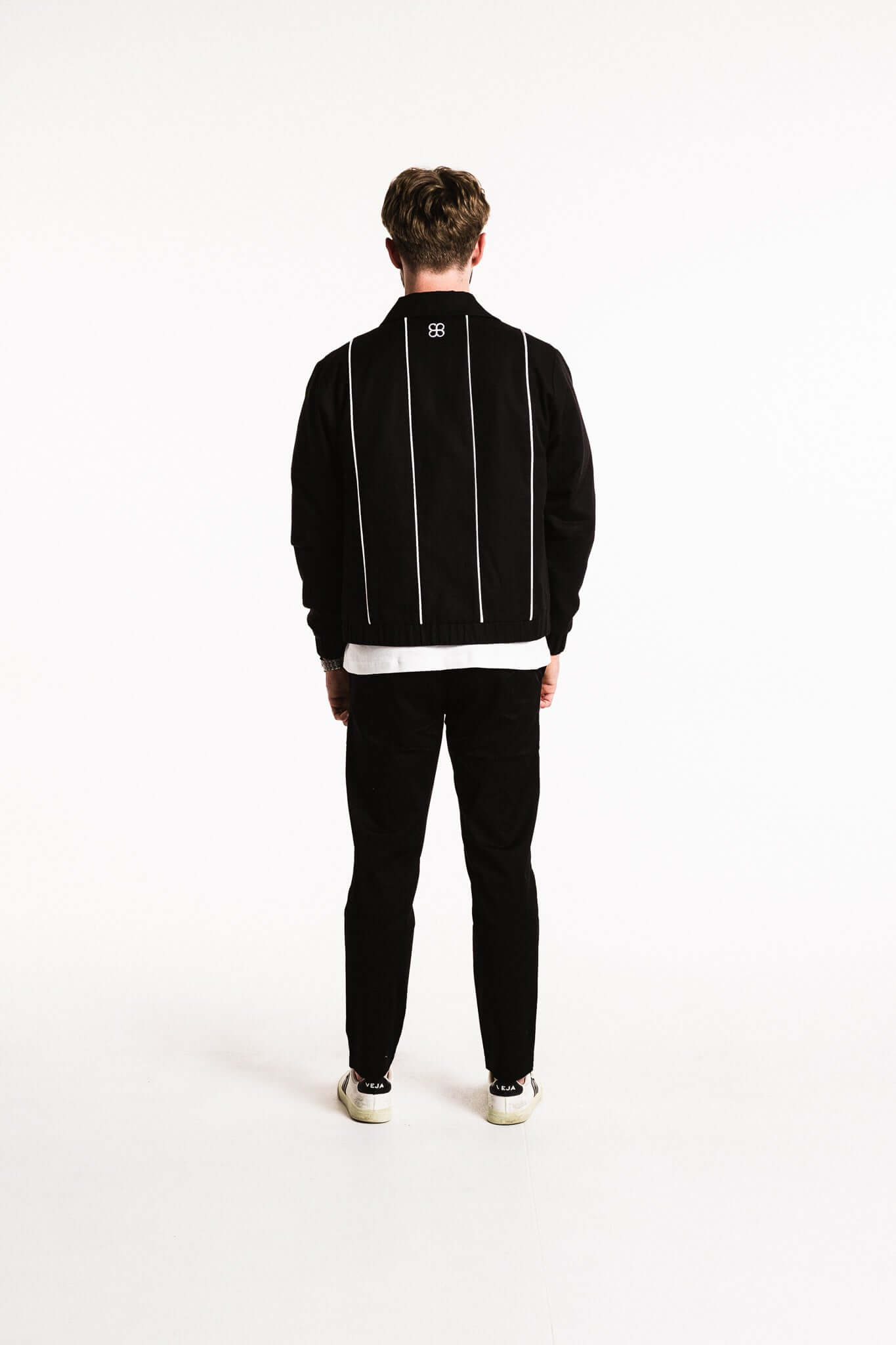 Back view of a model wearing a Cotton Contrast Jacket in Black with white piping and structured silhouette.