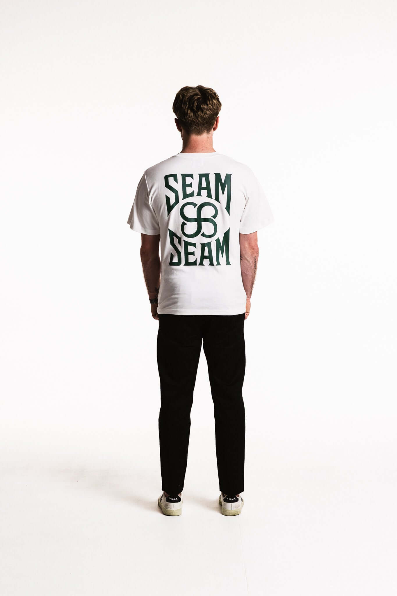 Cotton Typeface T-Shirt featuring bold SEAM branding on the back and minimal monogram on the chest, model view from rear.