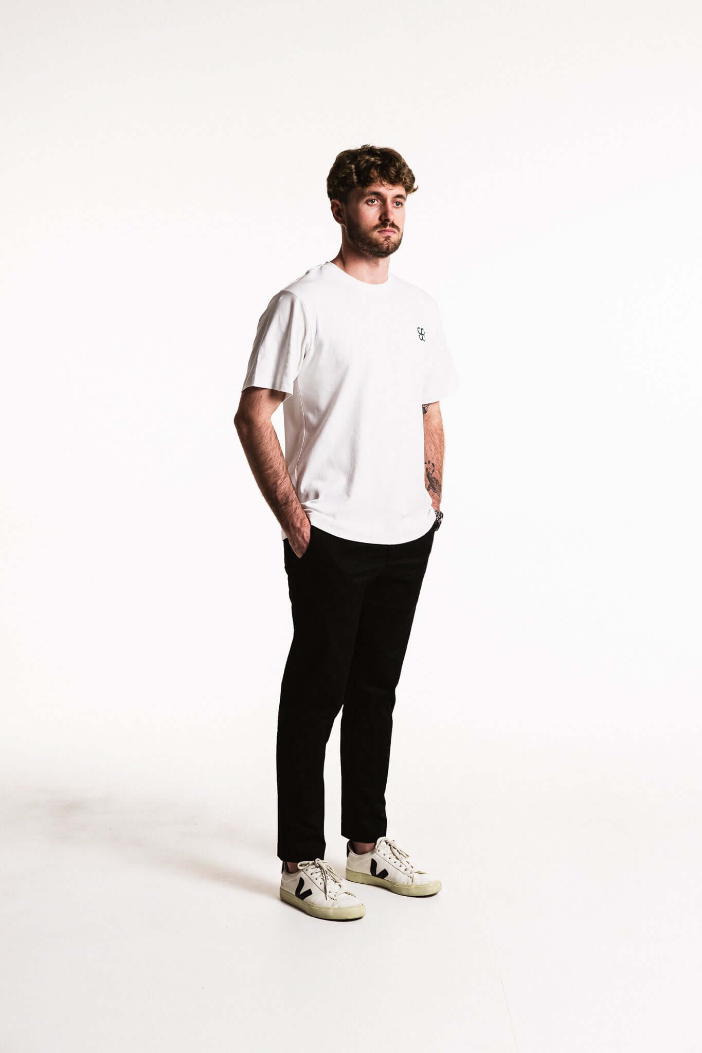 A man wearing a Cotton Typeface T-Shirt in white with relaxed fit and bold branding, paired with black pants.
