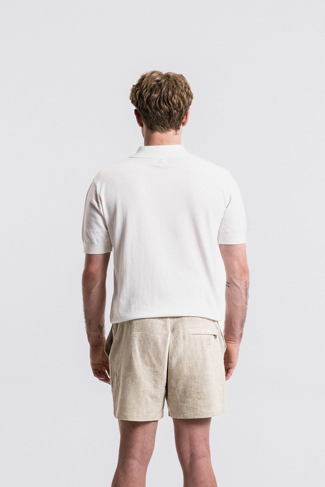 Man wearing a white polo shirt and beige shorts against a plain background