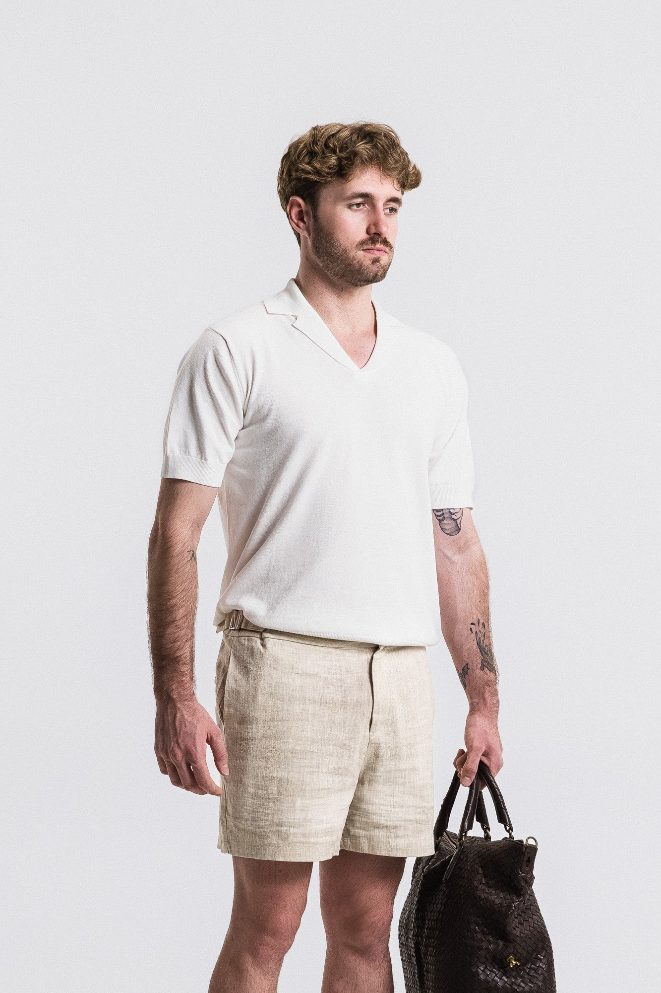 Man wearing a white shirt and beige shorts holding a bag against a plain background