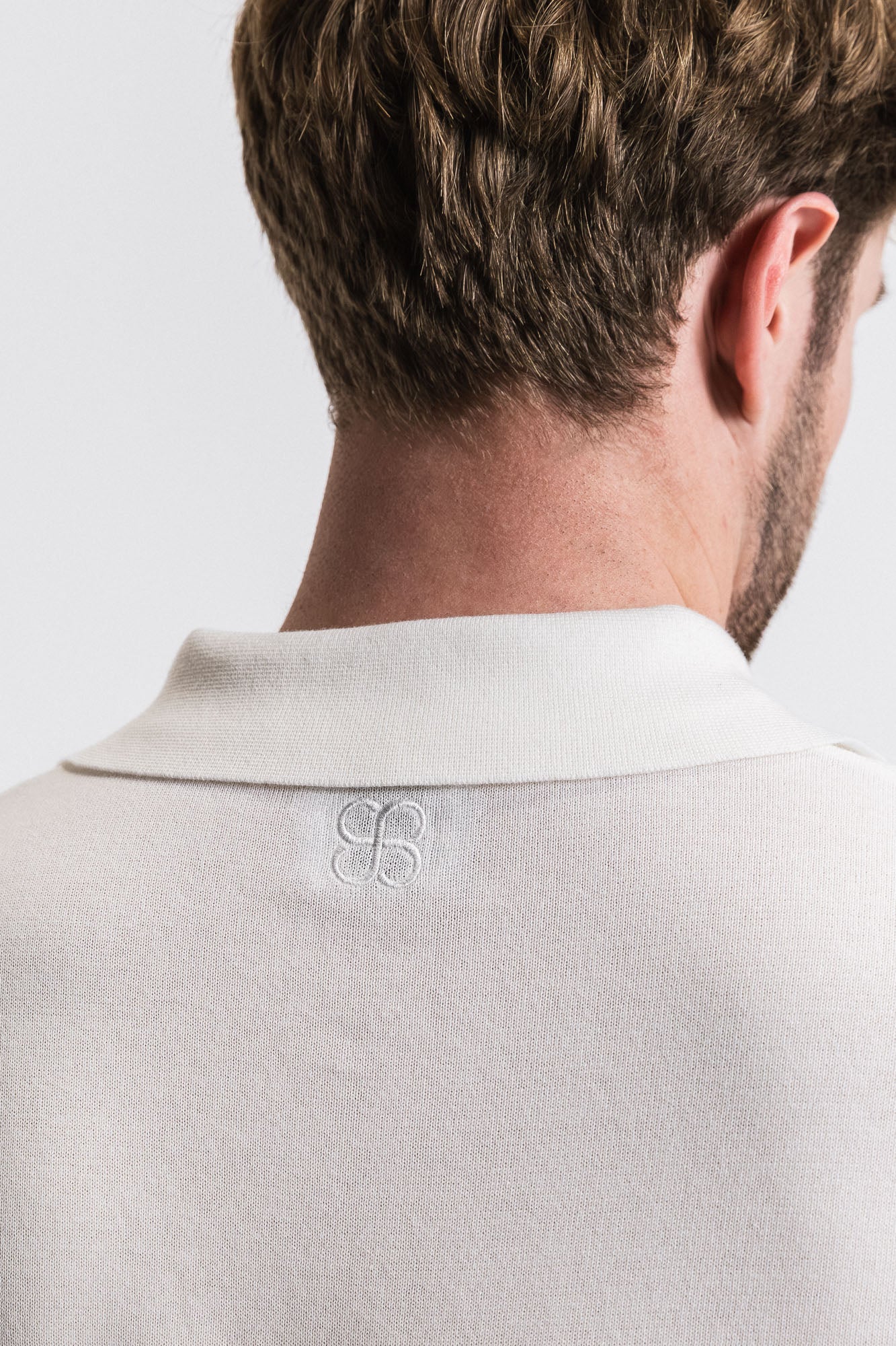 Close-up of a light gray shirt with a logo on the collar against a white background