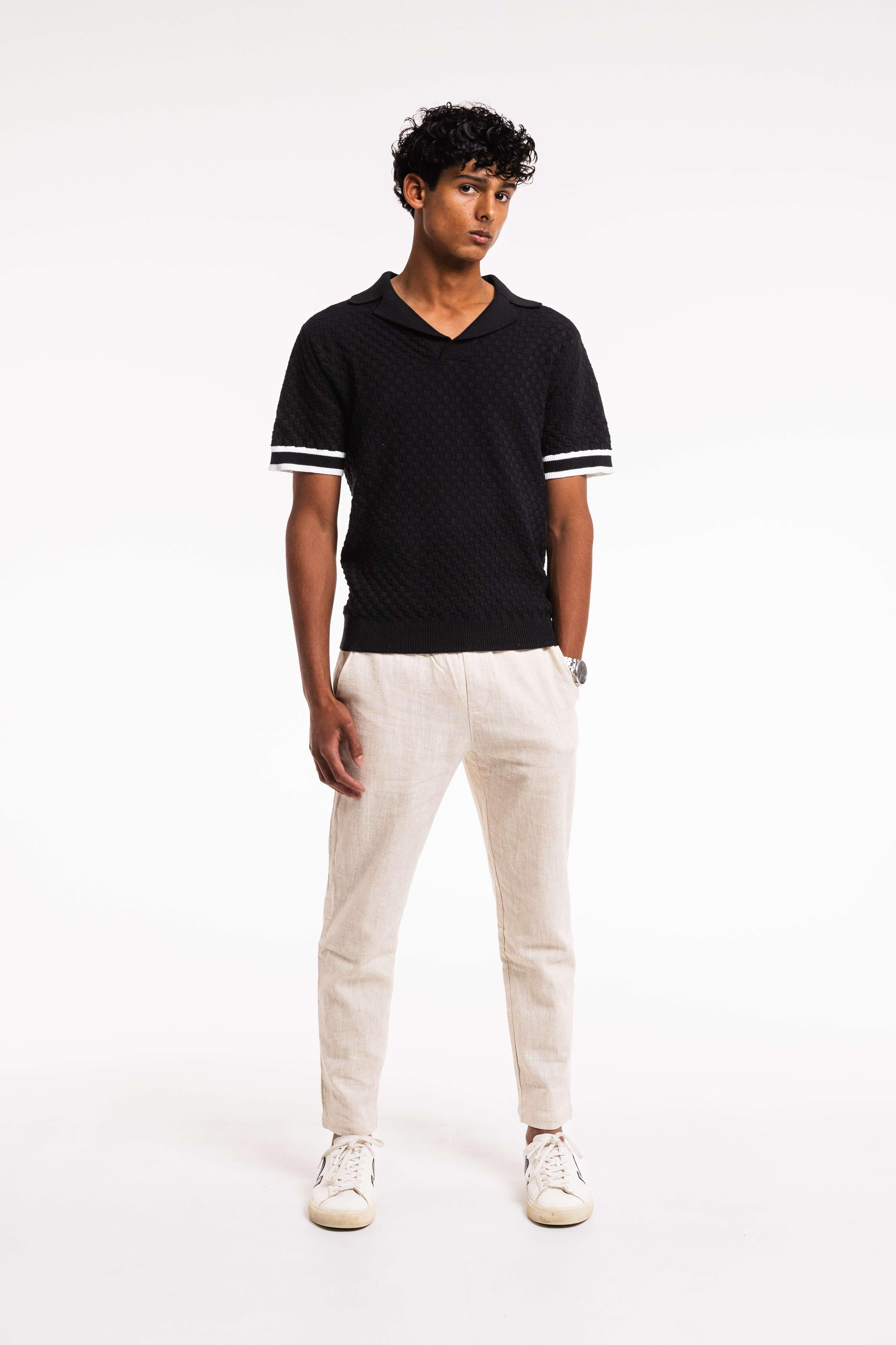 Man wearing a Checkered Cotton Knit Polo in Obsidian with contrast sleeve stripes and light-colored pants.