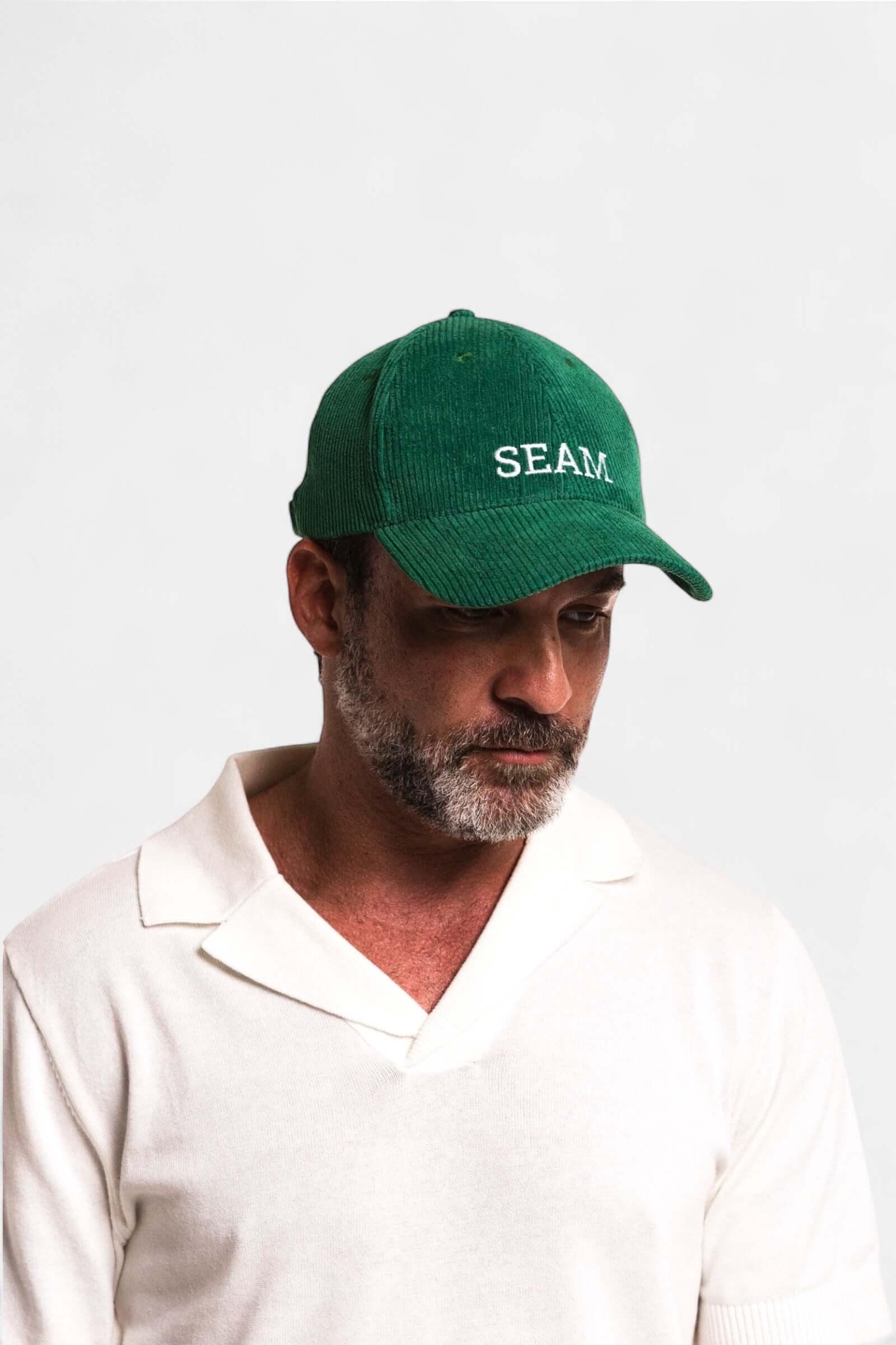 Seam Corduroy Logo Hat worn by a man, showcasing its forest green color and embroidered 'SEAM' detail.