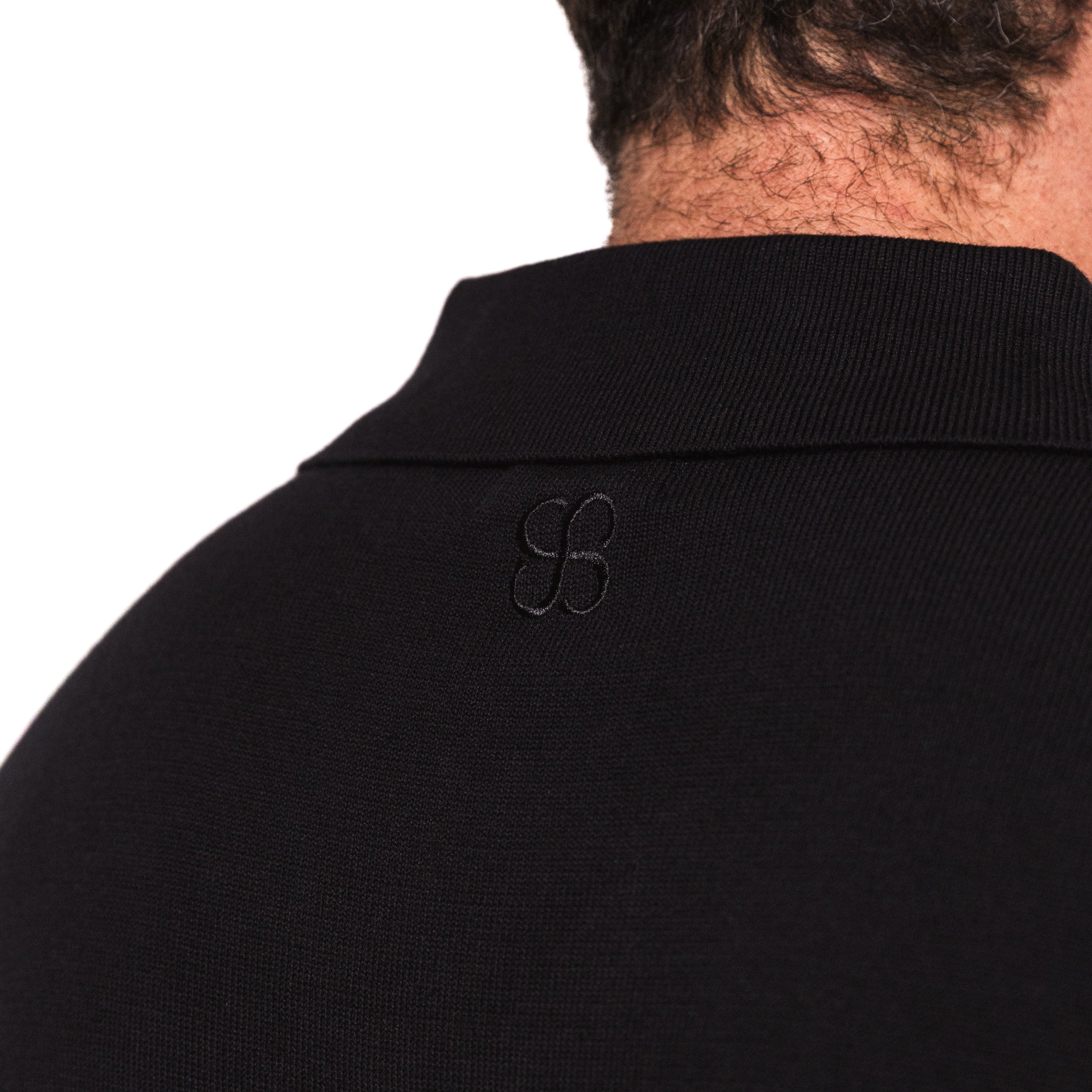 Black polo shirt with a logo on the collar against a white background