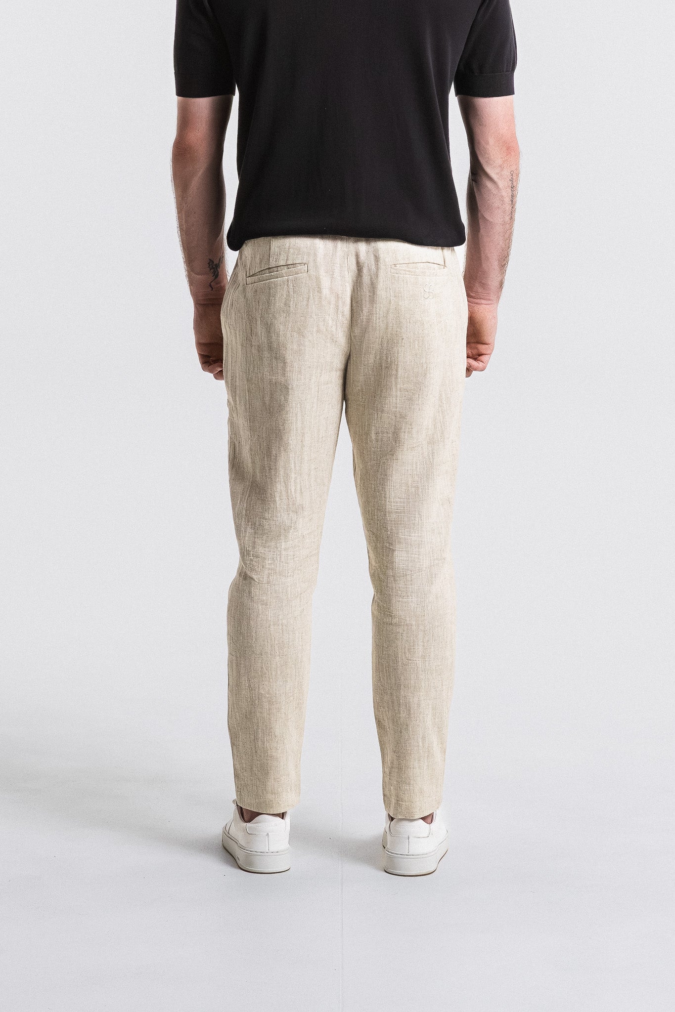Person wearing beige linen pants and a black shirt on a white background