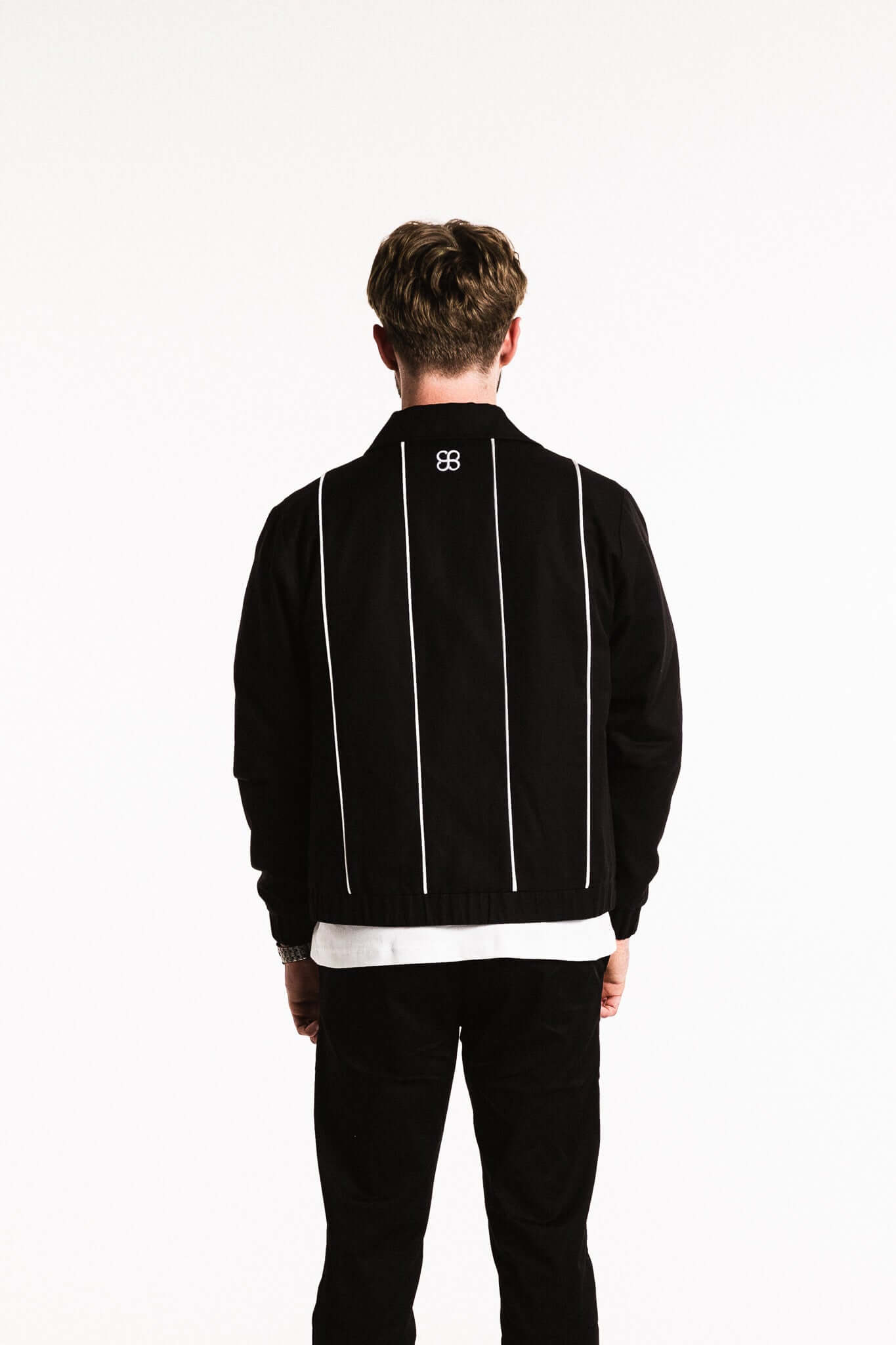 Back view of a man wearing a Cotton Contrast Jacket in Black with white piping details.